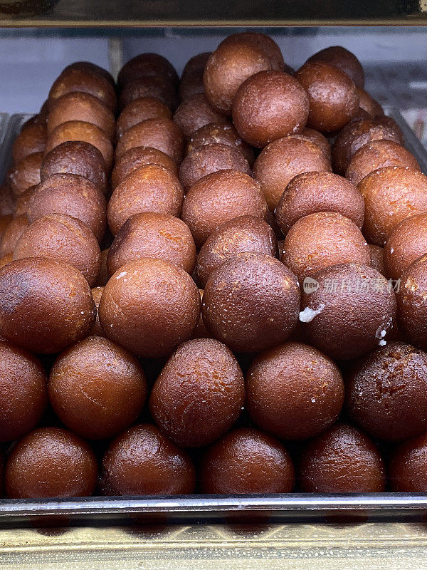 印度糖果店陈列的一盘“玫瑰水莓”(Gulab jamun) Mithai(糖果)的特写图片，前景是浸泡在玫瑰水糖浆中的khoya面团(干燥的淡奶固体)球